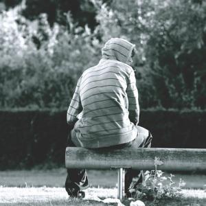 Ungt menneske´i stribet hættetrøje med ryggen til, der sidder på en bænk og kigger ud til højre.